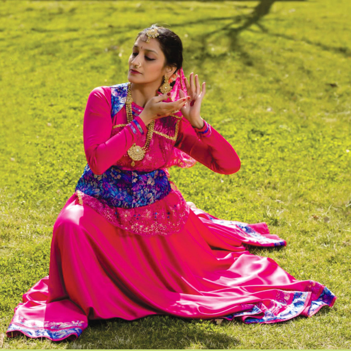 La danseuse Astha Godbole Karlekar en costume color&eacute; et en mouvement, assise sur une pelouse - portrait