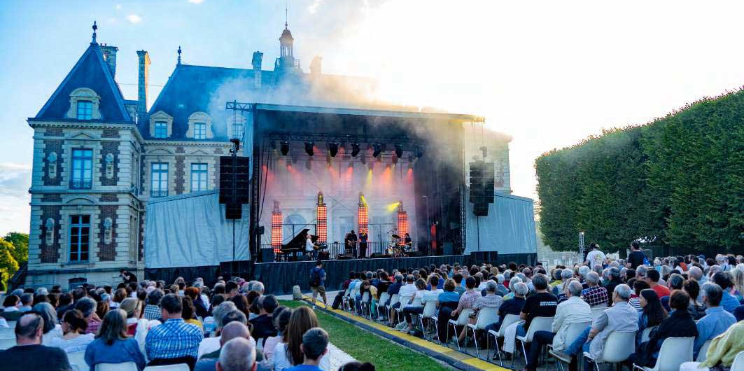 Festival Sceaux Jazz devant le Ch&acirc;teau de Sceaux, public devant la sc&egrave;ne en soir&eacute;e, ch&acirc;teau en fond de d&eacute;cor, fum&eacute;es color&eacute;es sur la sc&egrave;ne