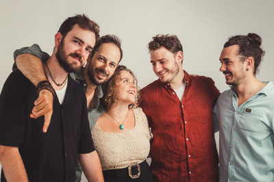 La chanteuse Lou Rivaille au milieu de son groupe de 4 musiciens Elle regarde l'un d'eux, les autres regardent l'objectif, tous sourient