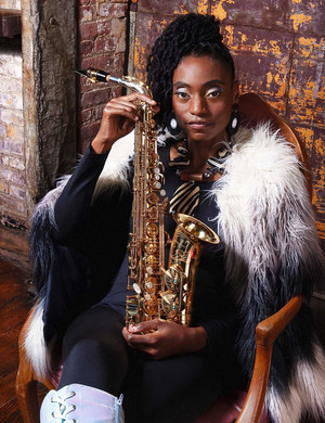 L'artiste Lakecia Benjamin assise, en habit de sc&egrave;ne (plumes, grandes bottes...) tenant son saxophone